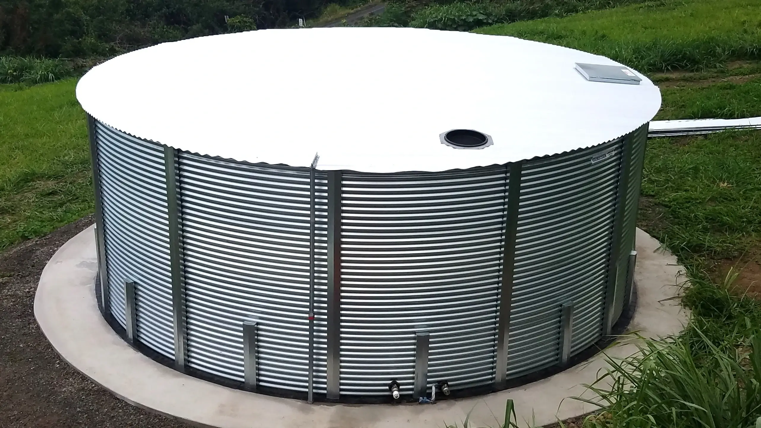 corrugated steel rainwater harvesting tank with white roof on concrete ring